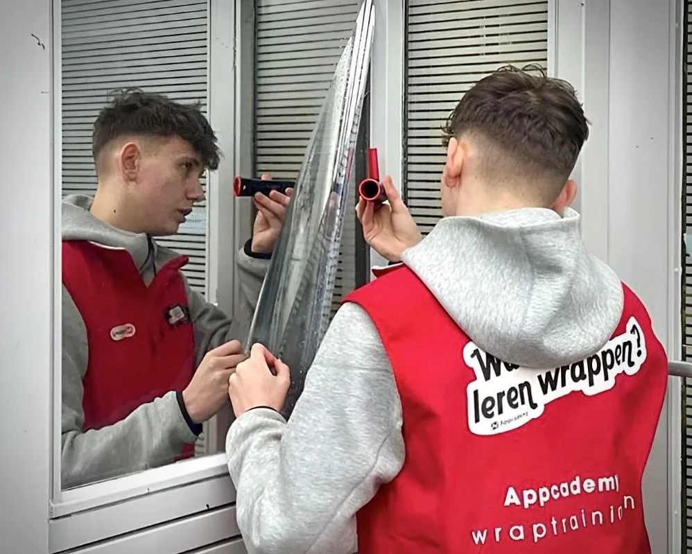 Cursist brengt raamfolie met gereedschap aan op ruit van gebouw tijdens Appcademy Architectural Windowfilm cursus