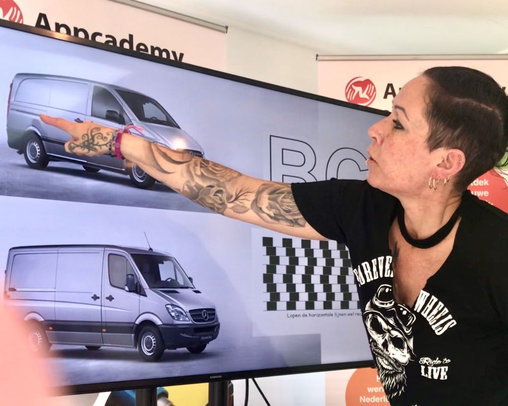 Cursist wijst naar een power point presentatie dia op een LCD scherm over het uitmeten van zelfklevende teksten en afbeeldingen op auto`s tijdens de Appcademy signmaker cursus opleiding