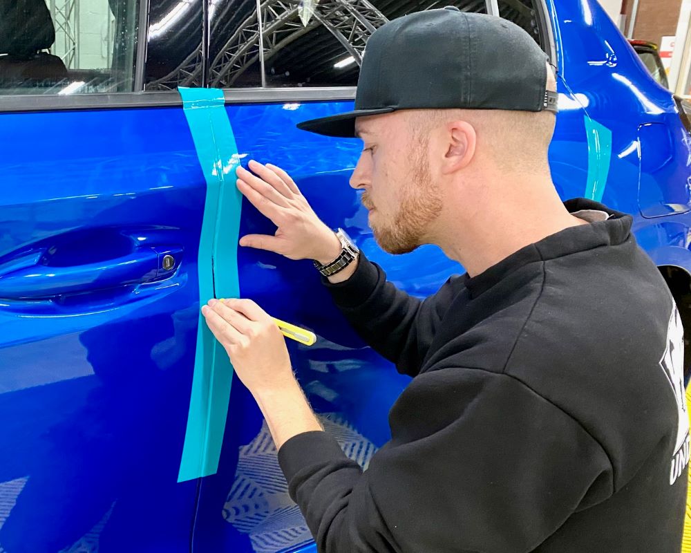 Een cursist leert in de praktijk hoe je folies afwerkt langs carrosserieranden tijdens de Appcademy signmaker training