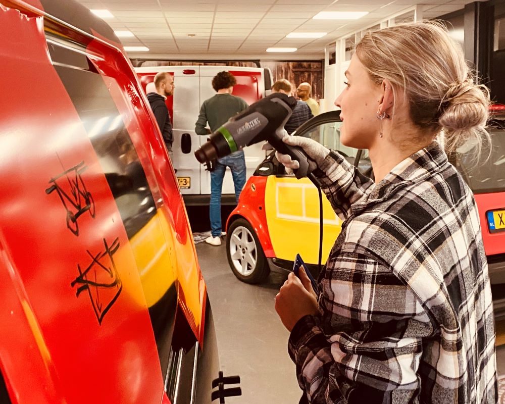 Cursisten wrappen printfolie en carwrapfolie als praktijk oefening in de diepe profileringen van bedrijfswagens tijdens Appcademy signmaker opleiding cursus