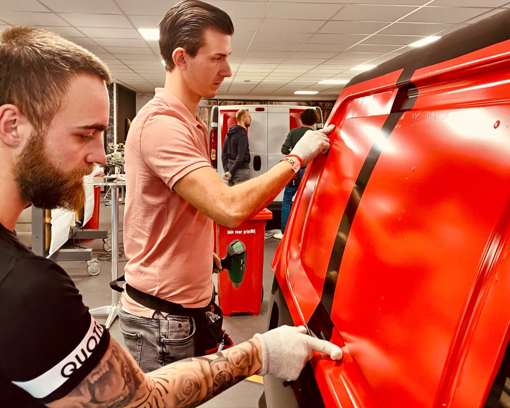 Cursisten wrappen zelfklevende folies in diepe profileringen bij bedrijfswagens tijdens Appcademy signmaker advanced beroepsopleiding