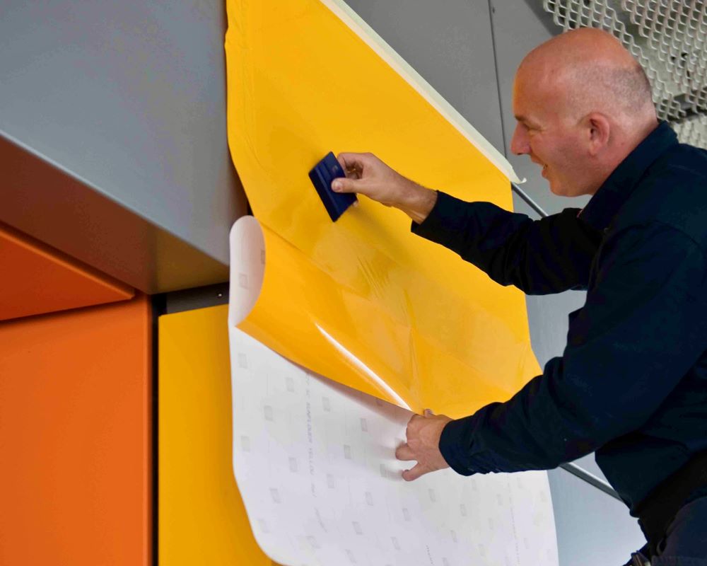 Man demonstreert plakken Facadefilm folie voor gevelelementen op een aluminium paneel