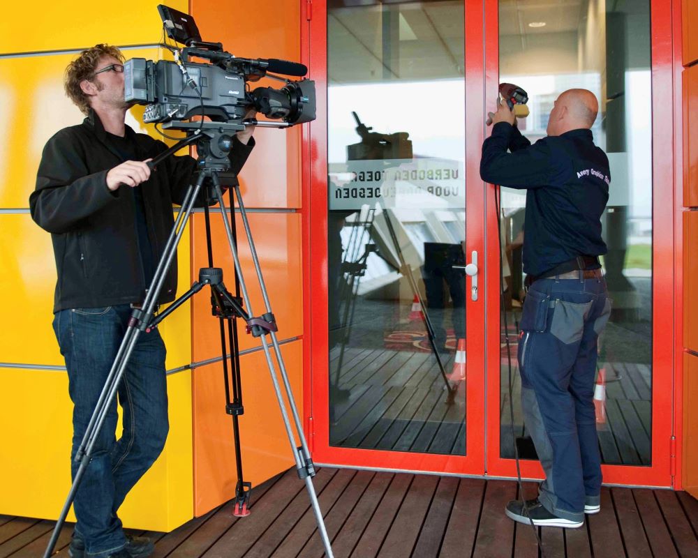 Man demonstreert aanbrengen Facadefilm kozijnfolie voor video opname met draaiende camera