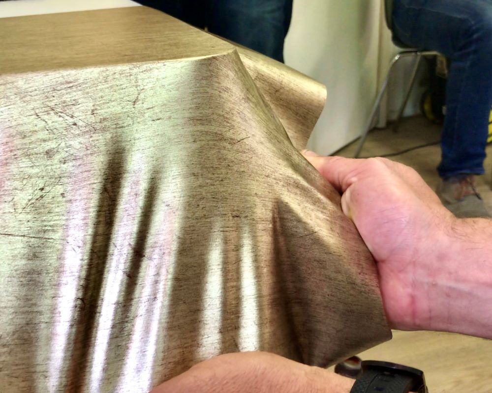 Cursist vormt interieurfolie verwarmd over de zijkanten van een tafelblad als praktijkoefening tijdens de Appcademy training interieurfolie en keukenwrap