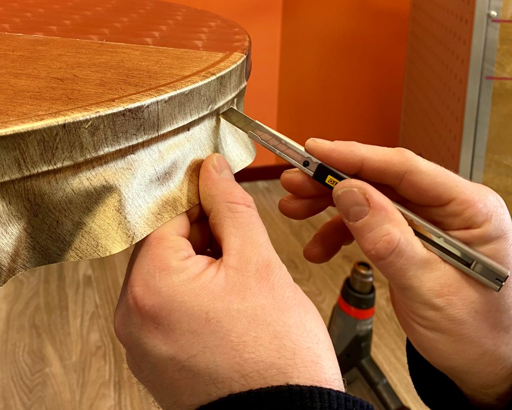 Cursist werkt de gewrapte zijkant van een bistrotafel af met snijtool als praktijkoefening tijdens de Appcademy training interieurfolies en keukens wrappen