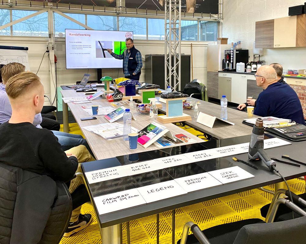 Gezelschap van trainer en cursisten aan tafel bij theorie gedeelte Appcademy Paint Protection Film opleiding