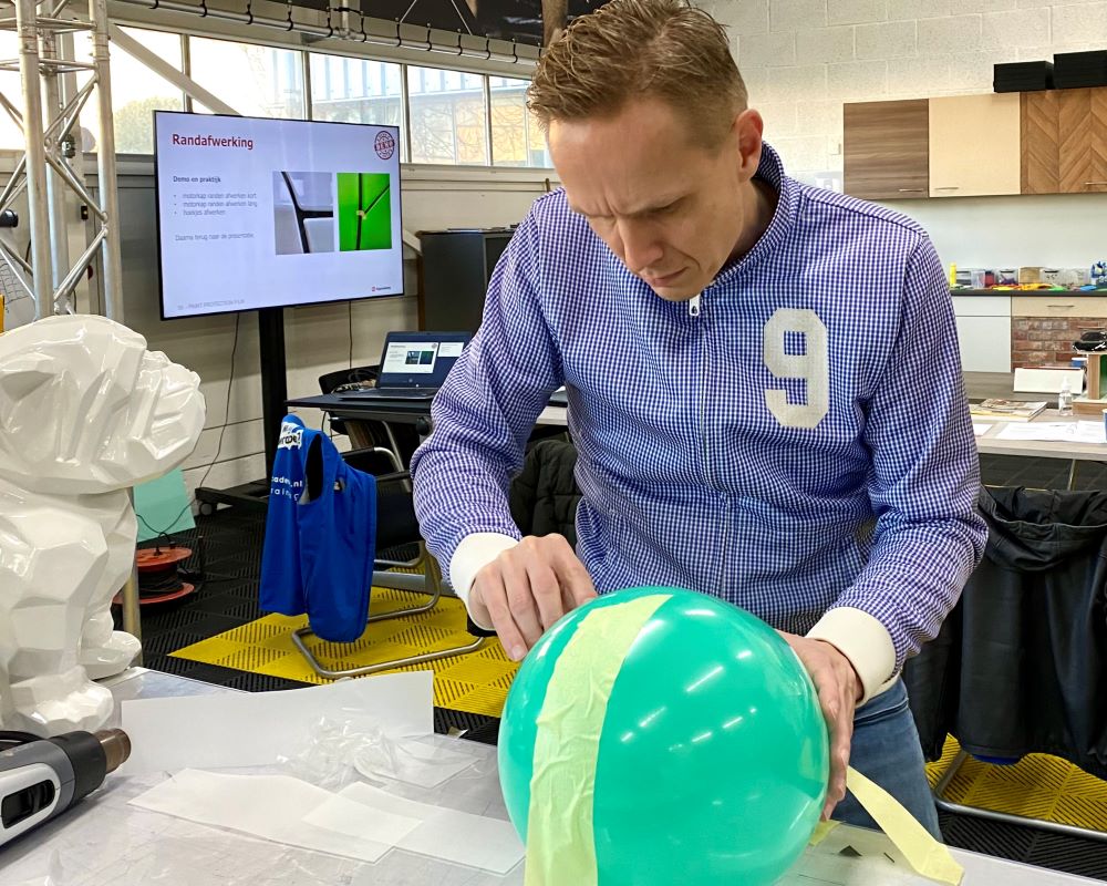 Cursist snijdt als praktijkoefening strookjes PPF folie op een opgeblazen ballon af tijdens Appcademy Paint Protection Film training