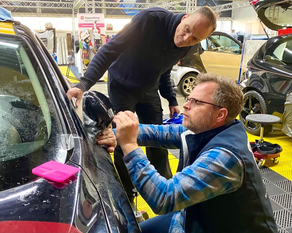 Trainer demonstreert plakken PPF op buitenspiegel van auto tijdens Appcademy Paint Protection Film opleiding