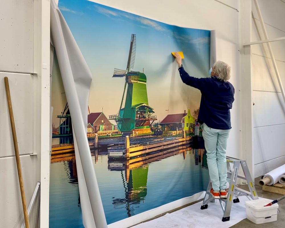 Cursist plakt geprinte afbeelding of print van een molen m.b.v. naadloos fotobehang op wand tijdens Appcademy Naadloos fotobehang cursus