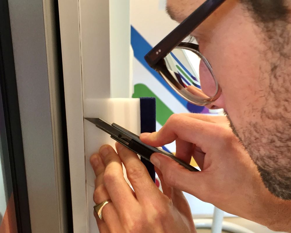 Cursist snijdt Facadefilm kozijnfolie langs de rakel af op binnenhoek aluminium kozijn tijdens “Schilderen met folie” Facadefilm training