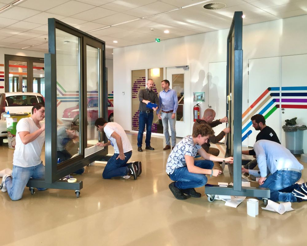 Cursisten doen praktijkoefeningen in de grote trainingsruimte met kozijnopstellingen tijdens “Schilderen met folie” Facadefilm training