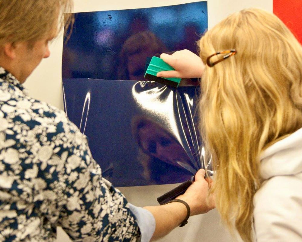 Trainer helpt student middelbaar beroepsonderwijs bij oefening folie plakken tijdens Appcademy workshop en gastcollege op ROC / MBO opleiding signmaker