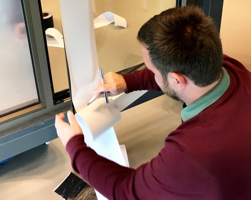 Cursist plakt Facadefilm kozijnfolie met rakel vast op aluminium kozijn tijdens “Schilderen met folie” Facadefilm cursus opleiding