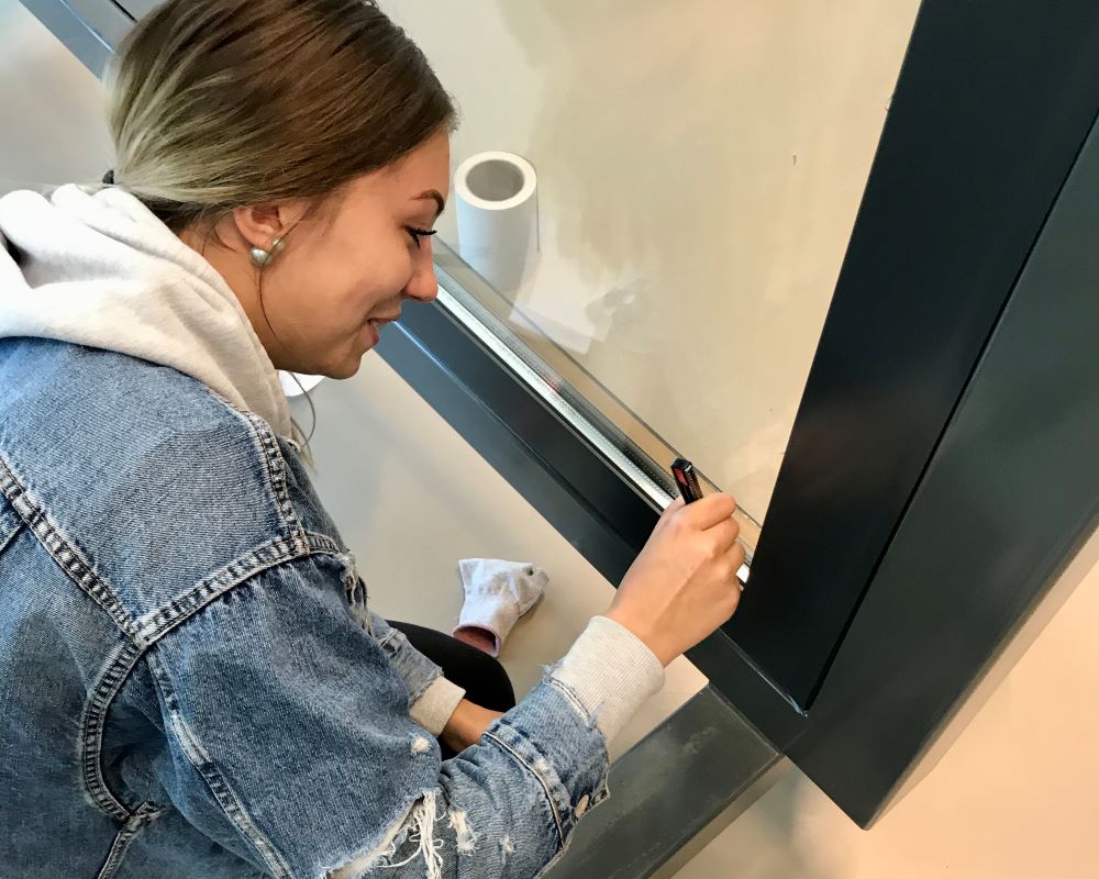 Cursist snijdt Facadefilm kozijnfolie met mesje af op aluminium kozijn tijdens “Schilderen met folie” Facadefilm cursus