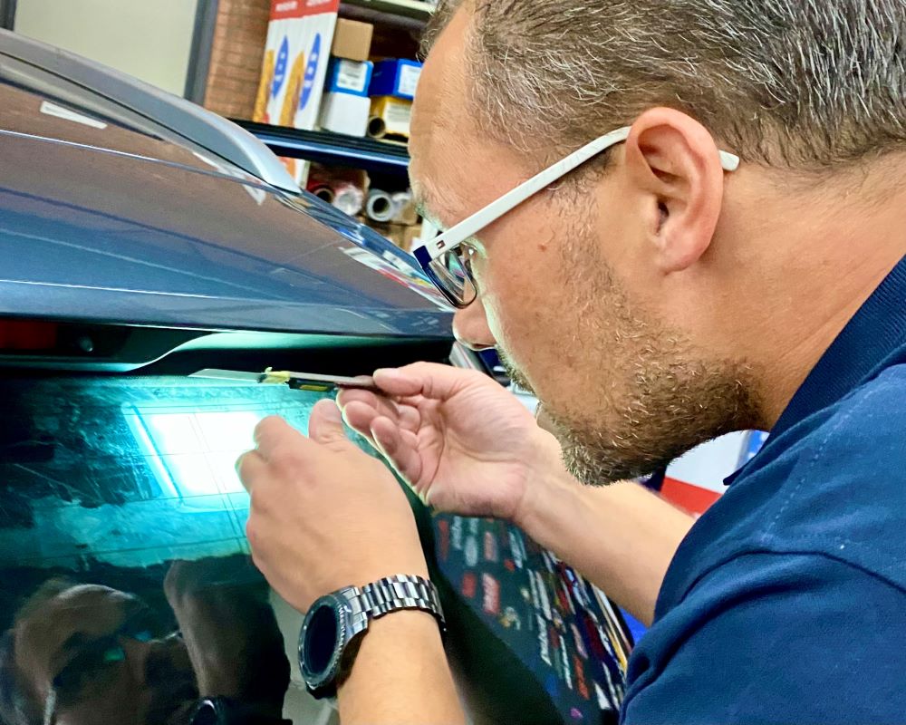 Trainer demonstreert het op maat snijden van raamfolie met tools zoals een mes en lamp tijdens Appcademy Automotive Windowfilm cursus