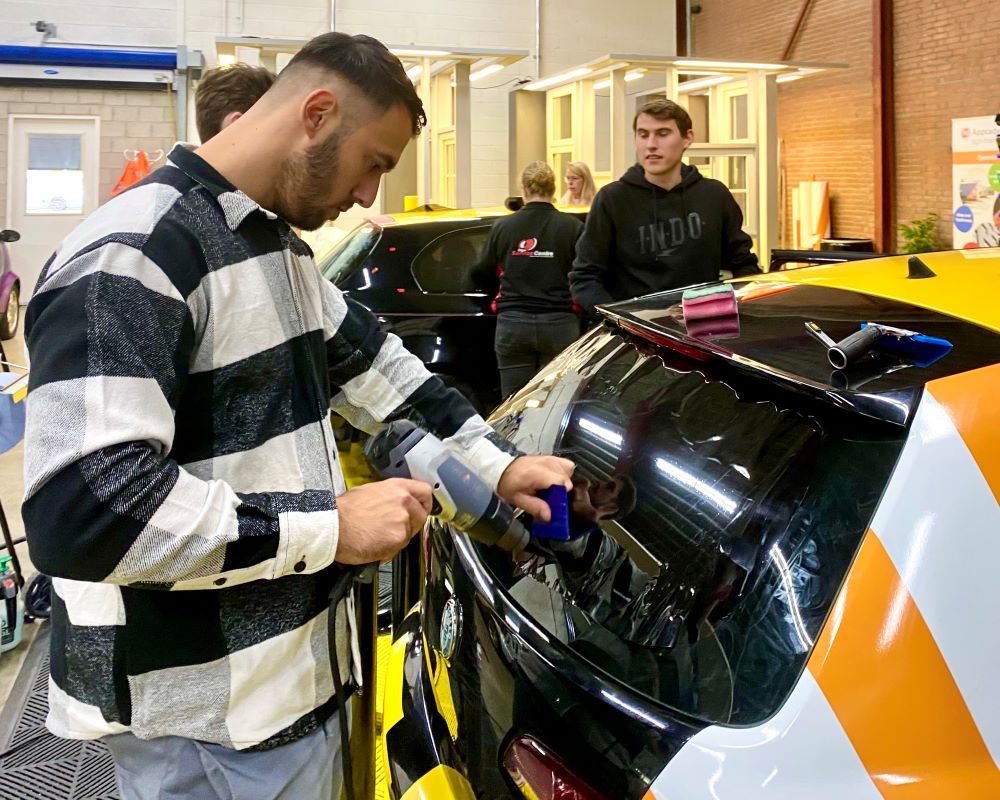 Cursist doet praktijkoefening raamfolie krimpen op bolle achterruit tijdens Appcademy Automotive Windowfilm training