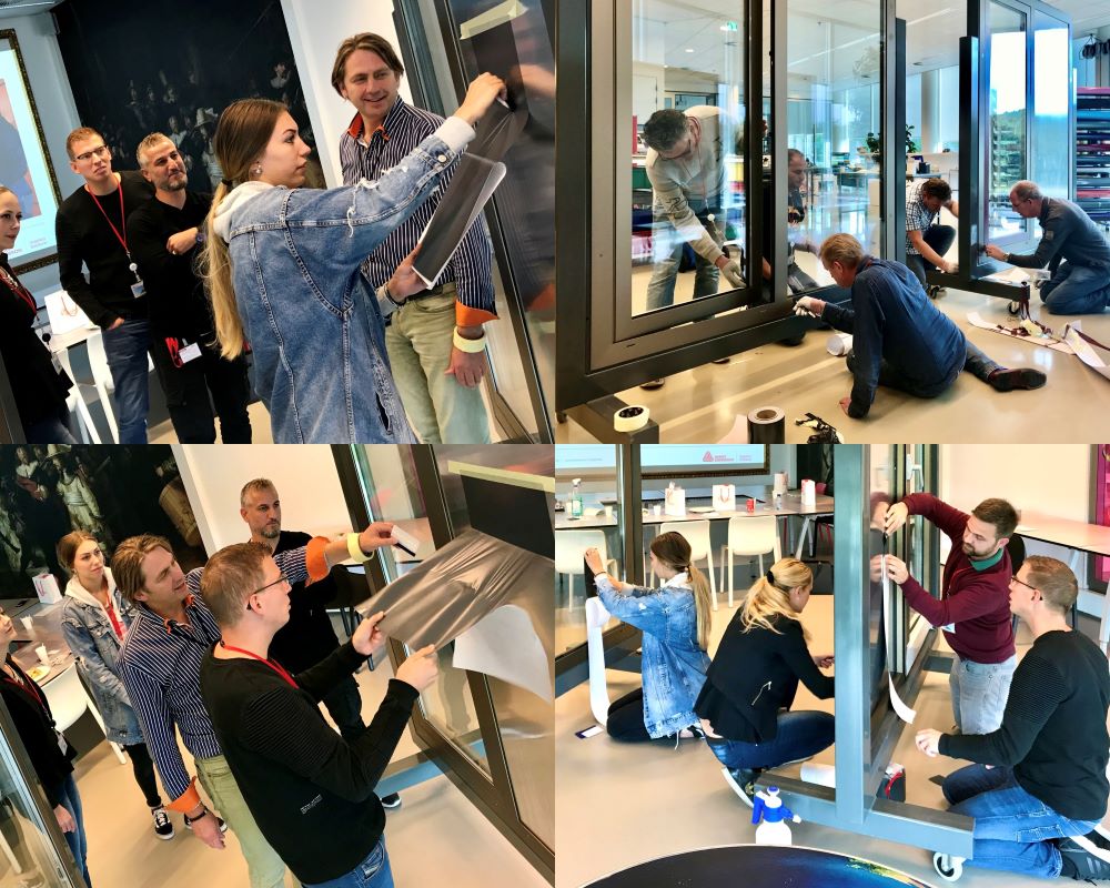 Cursisten doen praktijkoefeningen met kozijnfolie onder begeleiding van de trainer tijdens “Schilderen met folie” Facadefilm cursus opleiding