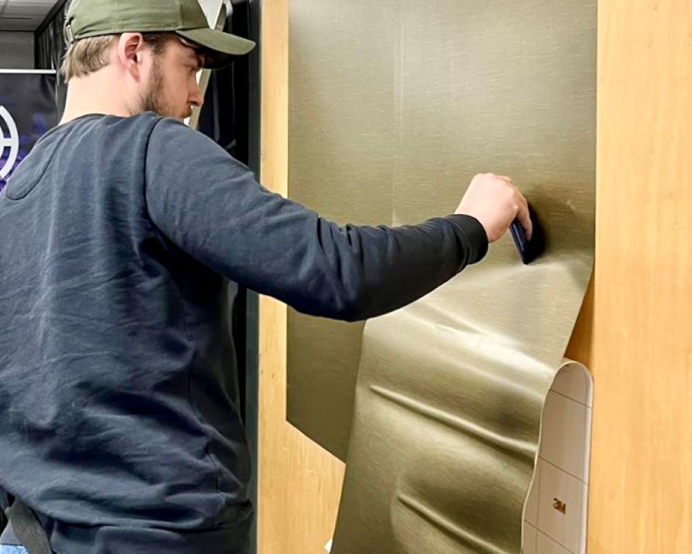 Cursist wrapt folie aan op wand tijdens de Appcademy cursus interieurfolie en keukens plakken